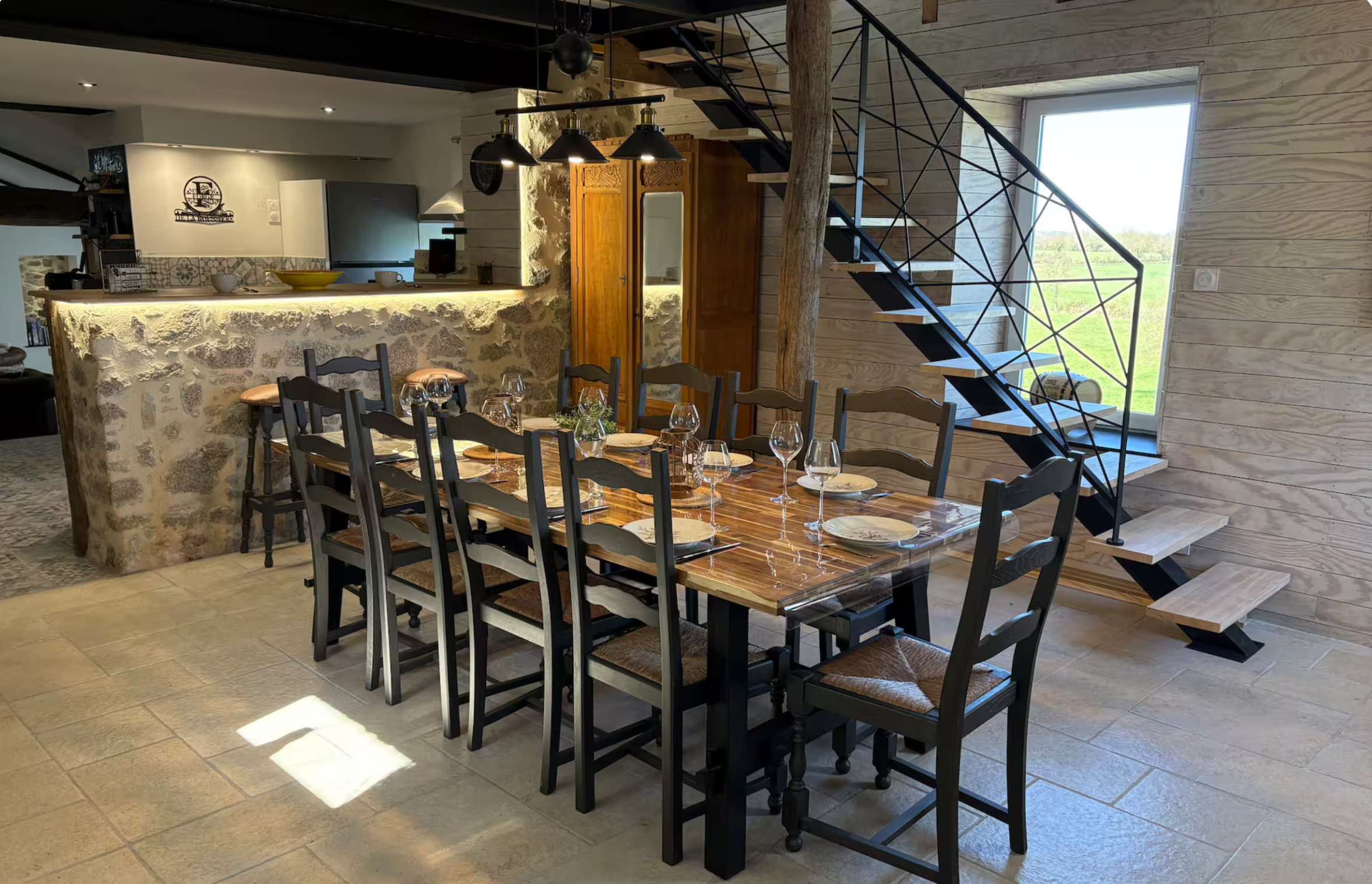 Salle à manger avec grande table en bois et escalier en métal noir